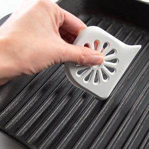 Cleaning the grooves of a grilling pan with the Rada Daisy PanMate Scraper.