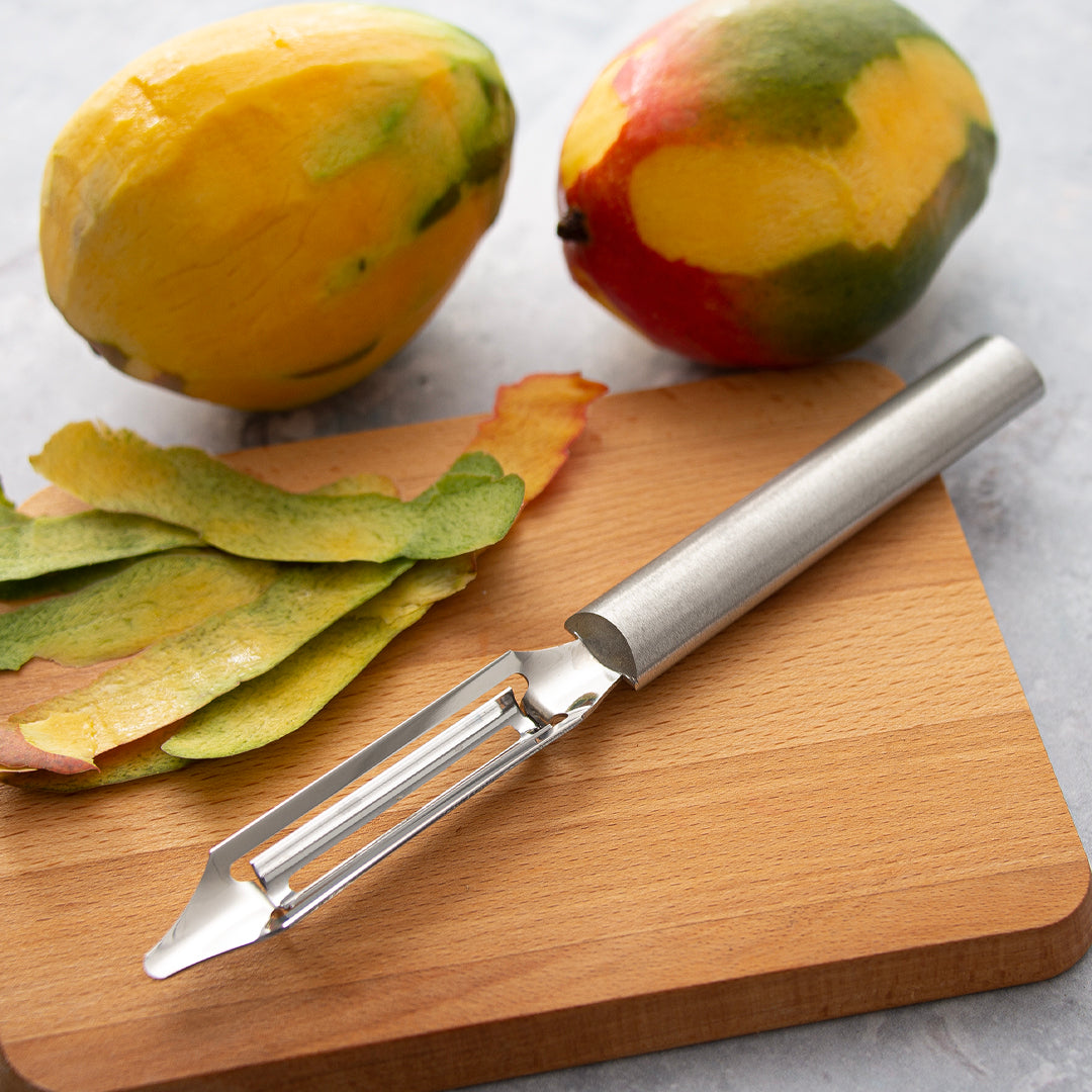 Rada's Silver handle Deluxe Vegetable Peeler on a cutting board with peeled and whole mangos.