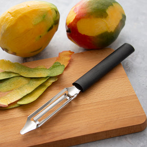 Rada's Black handle Deluxe Vegetable Peeler on a cutting board with peeled and whole mangos.