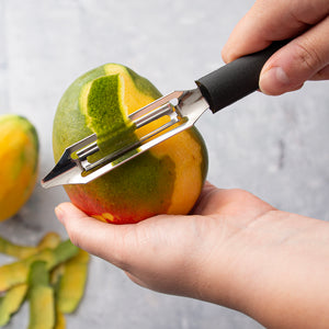 The Deluxe Vegetable Peeler peeling back the skin of a mango with an already peeled mango in the background.