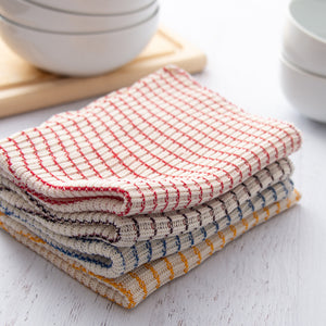 Stack of four dishcloths on a tabletop with cutting board and bowls in the background.