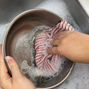 Dishcloth cleaning a bowl in the sink with soap and suds.