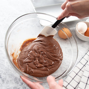 Mixing and scraping the side of a glass bowl filled with brownie batter with a Rada flexible spatula.