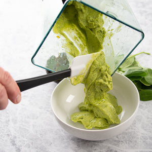 Scraping fresh-made spinach artichoke dip into a serving bowl using the Flexible Spatula with spinach leaves on the counter.