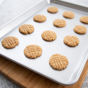 Half sheet pan full of peanut butter cookies on a wood cutting board and gray countertop.