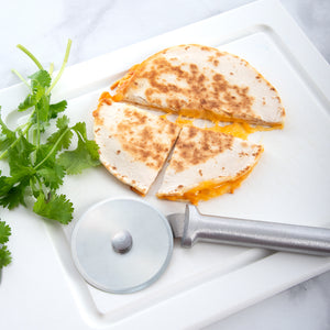 The Rada Cutlery pizza cutter laying on a plate with a sliced quesadilla. 