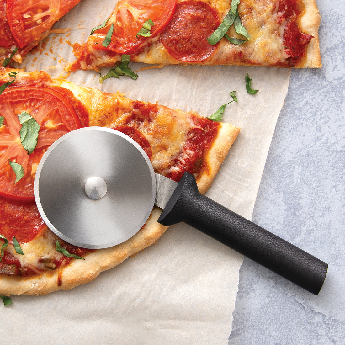Rada Cutlery pizza cutter with silver handle and steel wheel on pizza slice. 