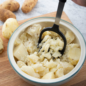 Mashing potatoes in a bowl, whole and peeled potatoes in the background.