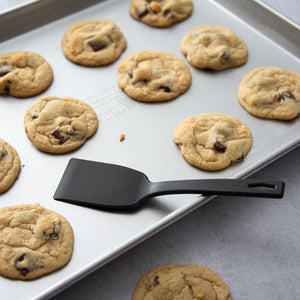 One of Rada's Potluck Spatulas laying on a sheet pan with chocolate chip cookies.