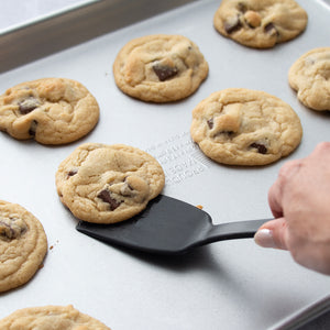 A Rada Potluck Spatula removing a chocolate chip cookie from a sheet pan.