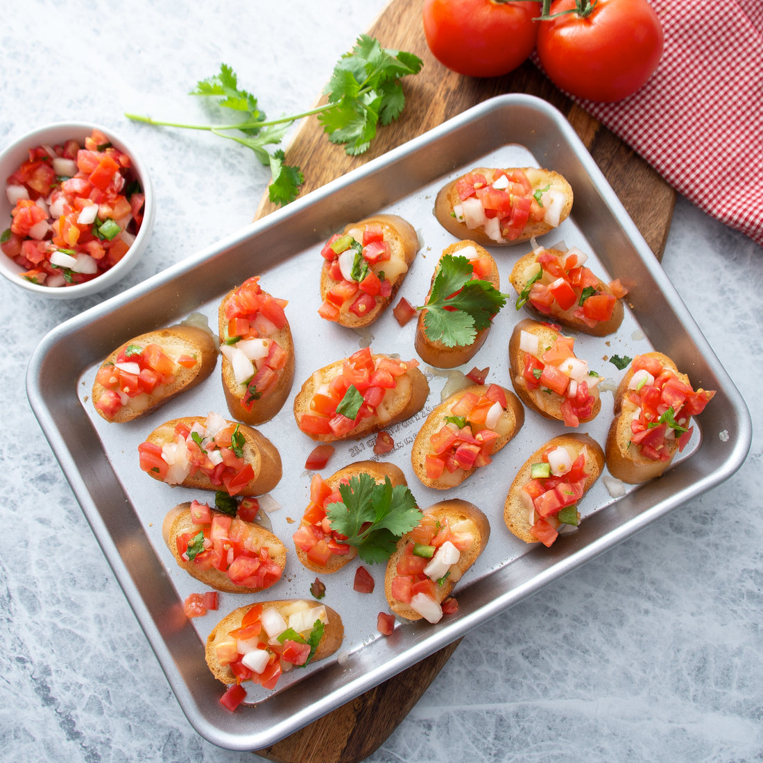 Quarter Sheet Pan filled with bruschetta on cutting board with tomatoes and basil.