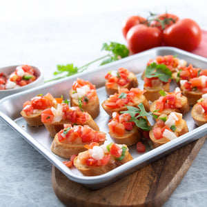 The durable 9 inch by 12.5 inch quarter sheet pan with Bruschetta appetizers on wooden board. 