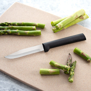 A black resin handled Rada Cutlery regular paring knife on a cutting board with cut asparagus. 