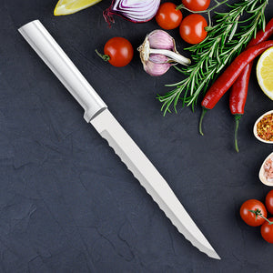 Rada's silver handle Serrated Slicer on a dark background with lots of vegetables next to the knife. Tomatoes, onions, peppers, and seasonings.