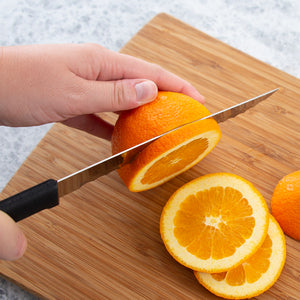 Serrated Slicer with black handle slicing an orange on a brown cutting board.