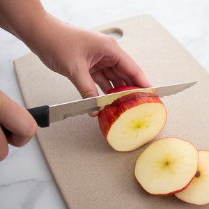 Rada's Black Handle Serrated Slicer slicing an apple on a cutting board with a white background.