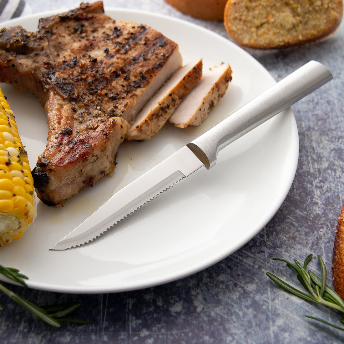 Rada Cutlery Serrated Steak Knife with silver handle on plate with sliced pork chop. 