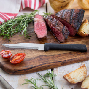 Serrated Steak Knife with black handle on wooden cutting board with sliced steak. 
