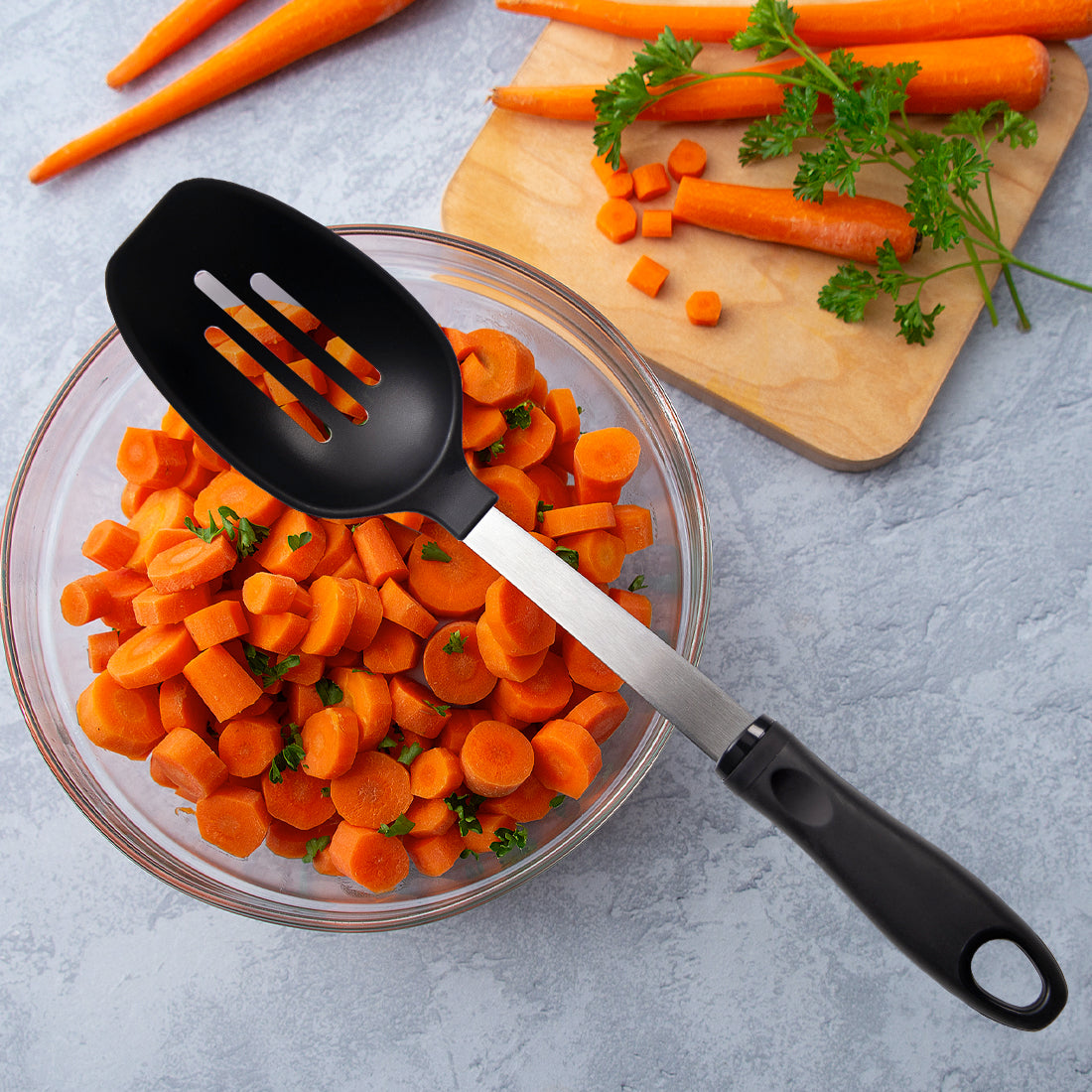 Chopped carrots with leafy greens, a cutting board and whole carrots with Rada's Basting Spoon.