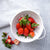 White colander full of strawberries next to a blue and white dishcloth.