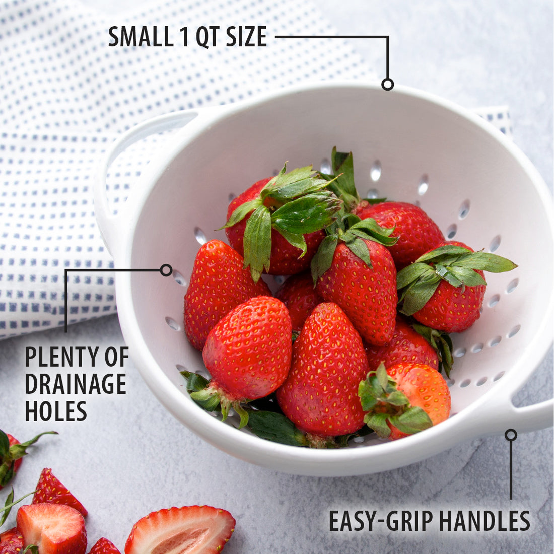 White colander full of strawberries next to a blue and white dishcloth.