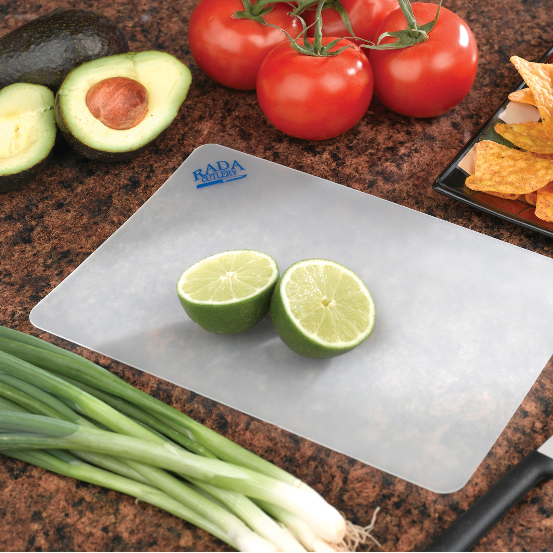 Lime halves on small plastic cutting board with green onions, avocados, tomatoes and Rada knife. 