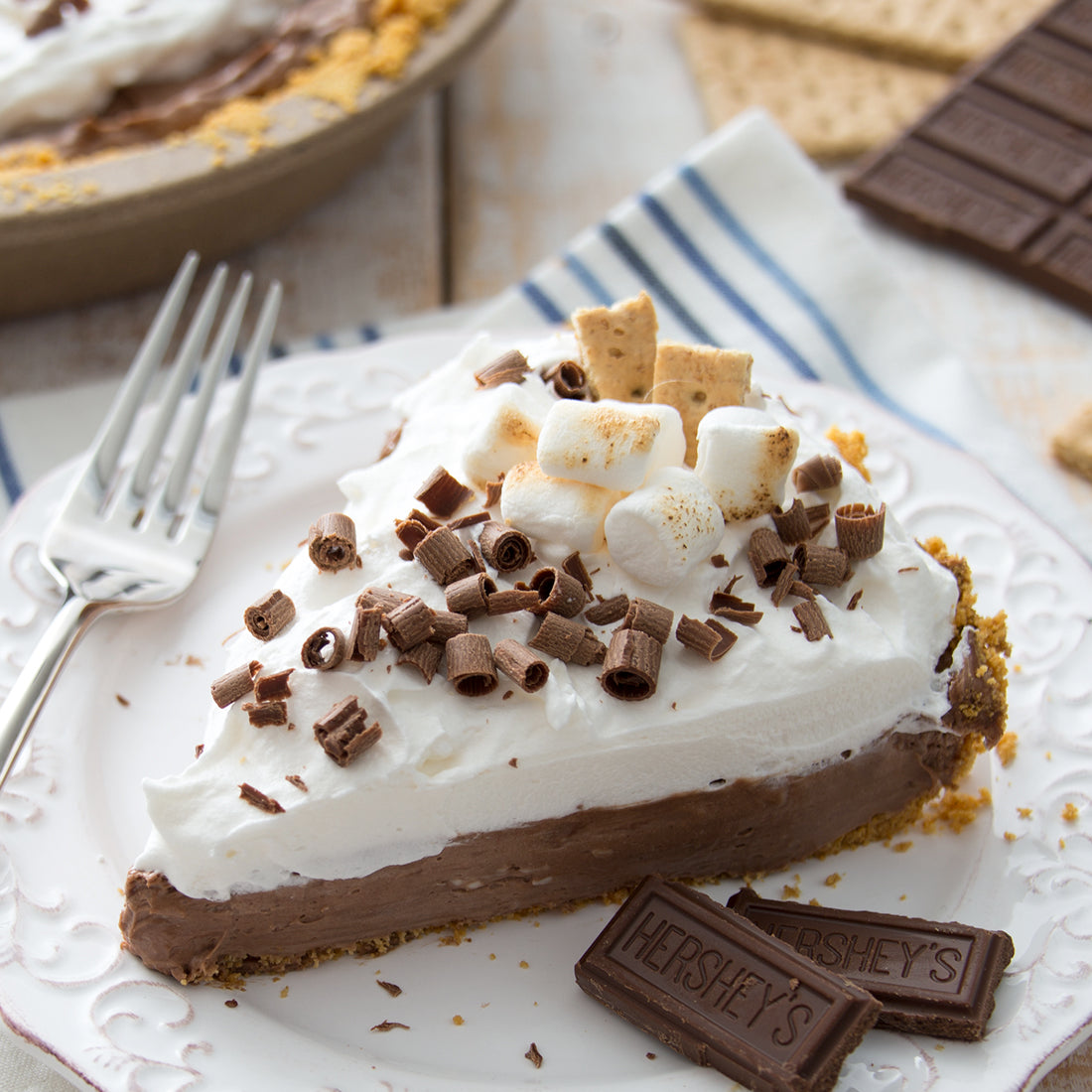 S'mores No-Bake Cheesecake in pie dish garnished with chocolate shavings and toasted marshmallows.