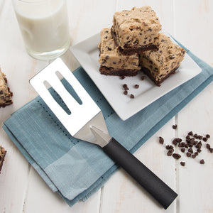 Spatula with black handle on blue napkin by chocolate chip bars stacked on plate. 