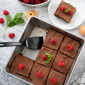 A square baking pan with brownies and raspberries. A brownie being served with Rada Potluck Spatula.