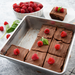 A square baking pan with frosted brownies topped with raspberries. White serving plate with brownie.