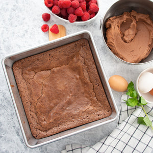 Baked brownies in Rada's 9" square baking pan, a bowl of chocolate frosting, and fresh raspberries. 