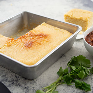 A square pan of baked cornbread being served with a bowl of black bean chili. 