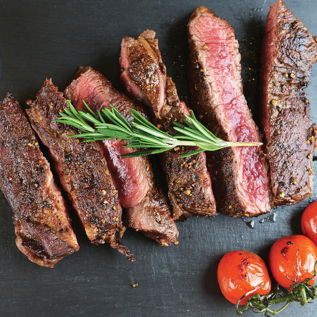 Steak & Chop Seasoning shown on sliced steak with blistered tomatoes and fresh rosemary. 