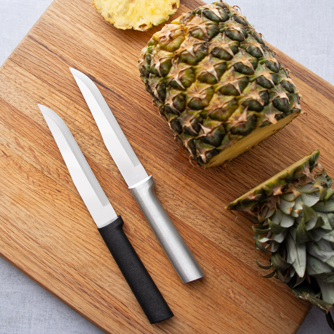 Silver and black handle Stubby Butcher laying on a cutting board next to a pineapple.