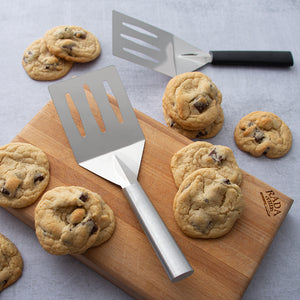 Silver and black handle Rada Turnovers with chocolate chip cookies on a cutting board.