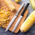 A silver and black handle Utility/Steak knife on a cutting board surrounded by whole and sliced corn.