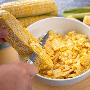A silver handle Utility/Steak knife slicing corn off a cob into a bowl for canning.
